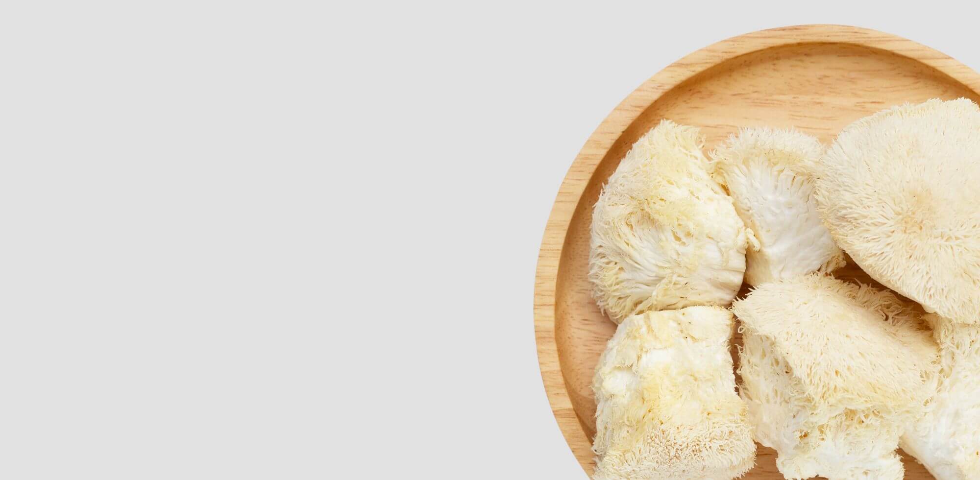 Lion's Mane (Hericium erinaceus) Pilze auf einem runden Holztablett, bekannt für ihre positiven Wirkungen auf Gehirnfunktion und Nervenregeneration – ideale Wahl für Vitalpilz-Anwendungen.