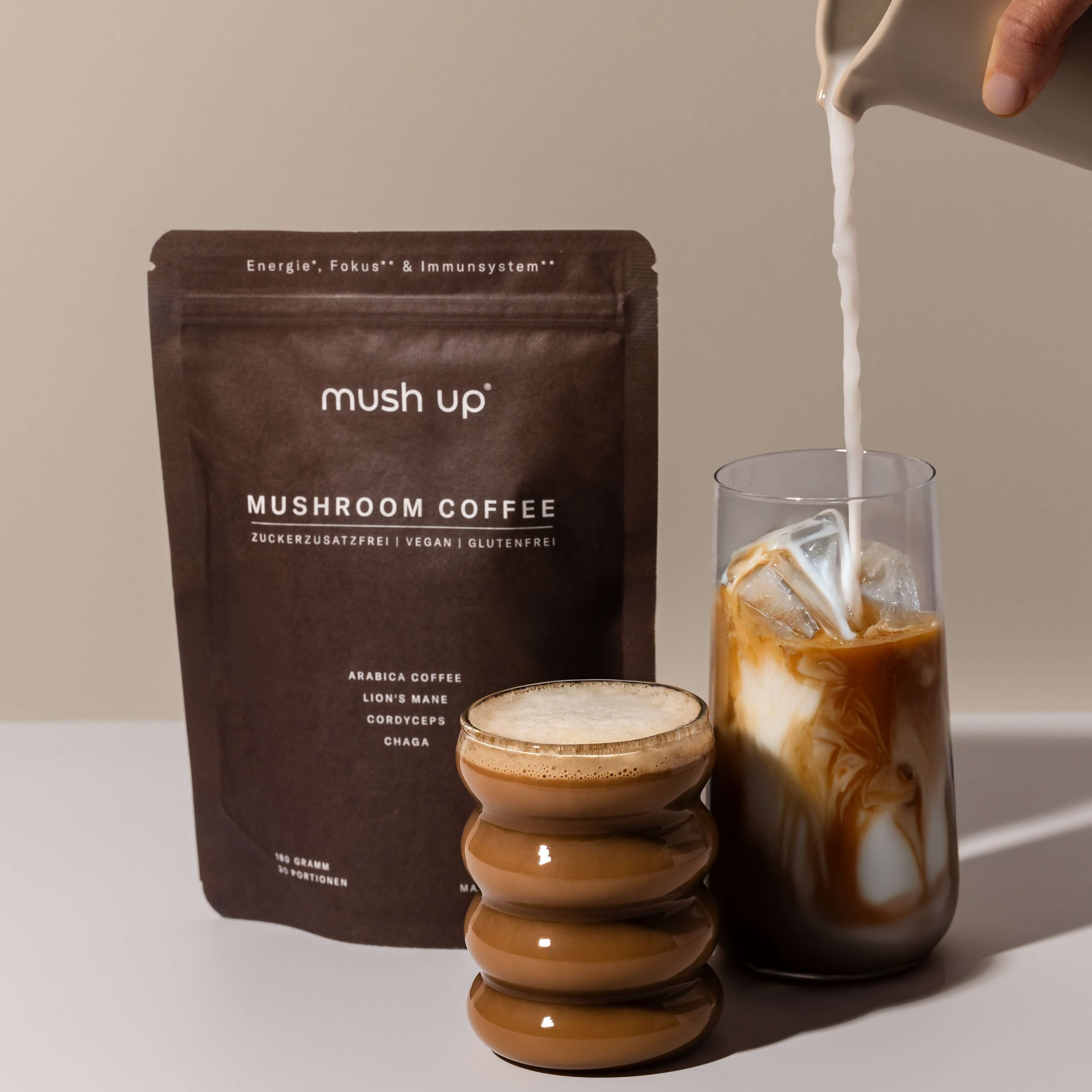 mush up Mushroom Coffee in der Zubereitung – Milch wird aus einer Karaffe in ein Glas mit Iced Mushroom Coffee gegossen, daneben eine Packung mit Lion’s Mane, Chaga und Cordyceps Heilpilz-Kaffeemischung.