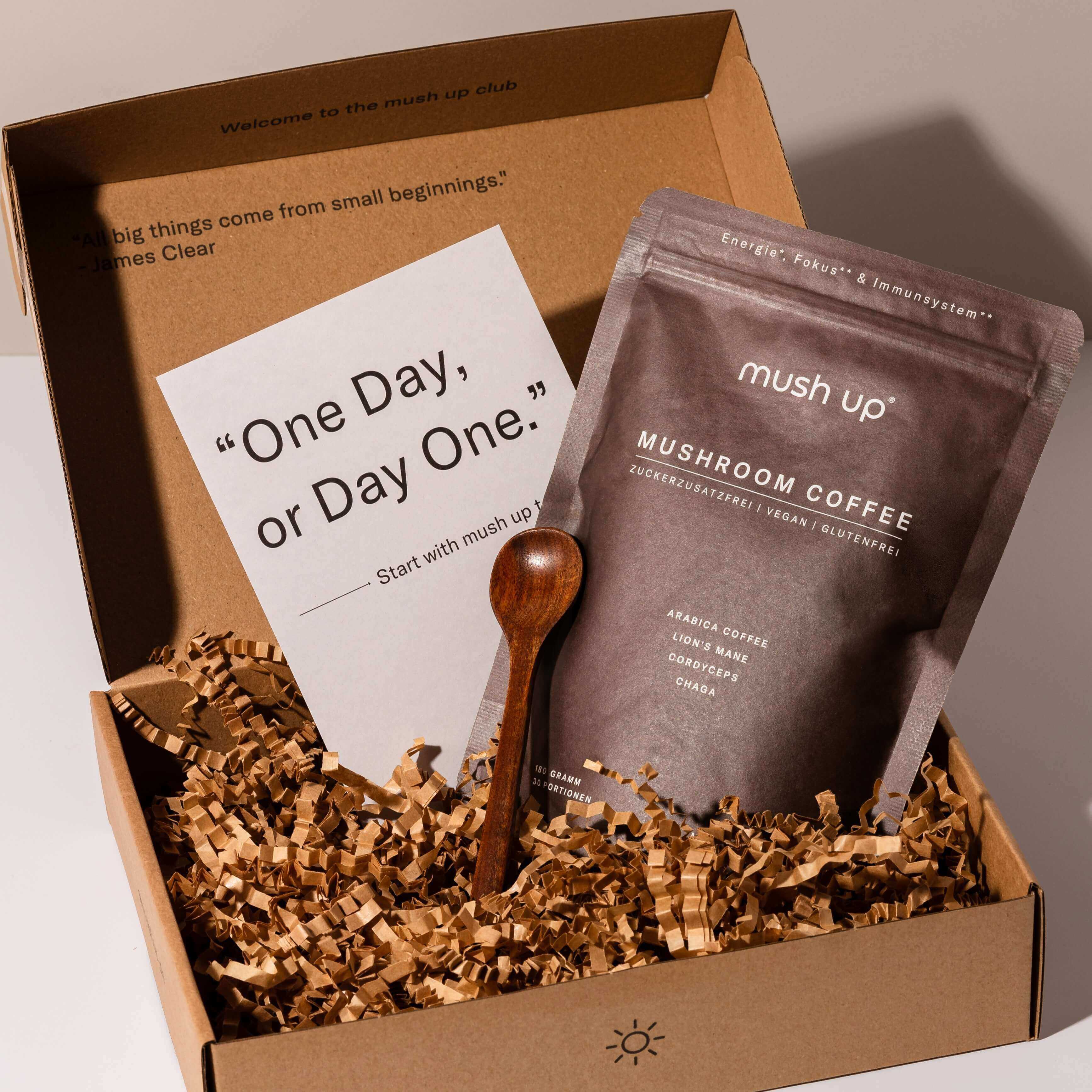 mush up Mushroom Coffee Starter-Set in einer stilvollen Verpackung mit motivierender Karte ‚One Day, or Day One.‘, einer Packung Mushroom Coffee mit Lion’s Mane, Chaga und Cordyceps sowie einem hochwertigen Holzlöffel.